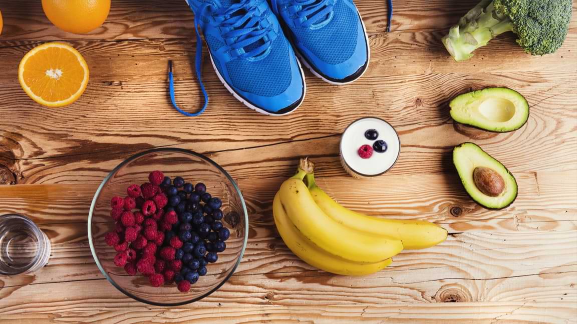 nutritious fruits and vegetables on a wood background with workout shoes on display showing food and exercise connection